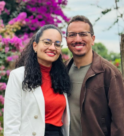 Fê e Naná sorrindo juntos em frente a um jardim florido